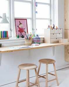 two wooden stools sitting on top of a desk in front of a large window