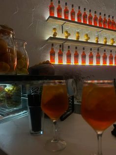 two glasses filled with liquid sitting on top of a counter next to bottles and jars