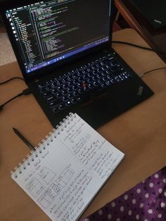 an open laptop computer sitting on top of a wooden desk next to a notepad