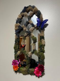 a mirror decorated with flowers and butterflies on the wall next to a white wall in a room