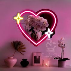 a heart shaped neon sign with flowers in the center on a shelf next to a potted plant