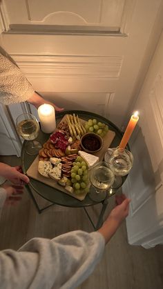 a tray with cheeses, crackers and grapes on it next to a candle