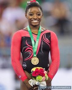 a woman in a black and red leotard with flowers on her lap holding a gold medal