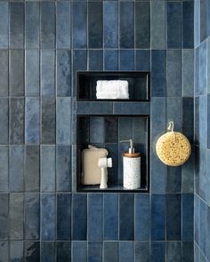 a blue tiled bathroom with two shelves and soap dispensers on the wall