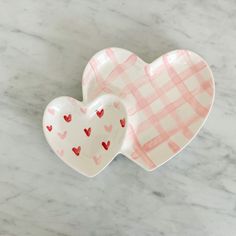 two heart shaped dishes sitting on top of a marble tablecloth covered counter with white and pink checkered paper