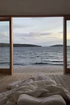 an empty bed is in front of large windows overlooking the water