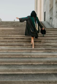 a woman is walking up some stairs with her hand in the air and wearing a black coat