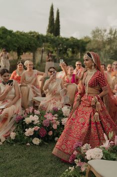 a woman in a red and gold wedding dress standing next to other women sitting down