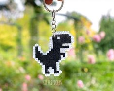 a hand holding a pixelated keychain with a small black dinosaur on it