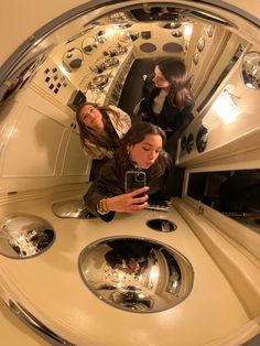 three women are looking at their cell phones in the reflection of another woman's mirror