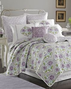 a white bed with purple and green comforter in a room next to a window