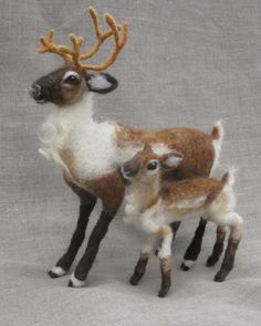 two miniature deer standing next to each other on a gray surface with white and brown fur