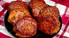 four pieces of meat sitting on top of a black plate with red and white checkered table cloth