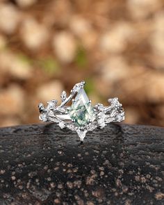 an engagement ring with a pear shaped green diamond surrounded by leafy branches on a rock