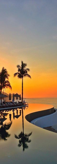 the sun is setting over an empty swimming pool with palm trees in the foreground