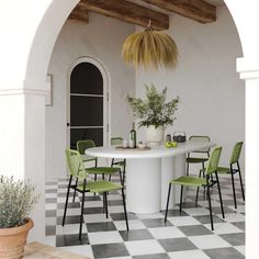 a white table with green chairs and a potted plant in the center is surrounded by black and white checkered tiles