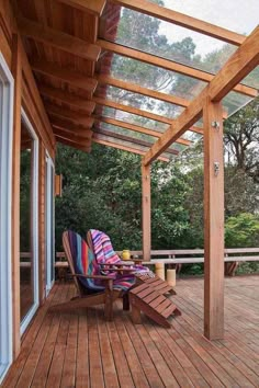 a wooden deck with a chair and table under a pergolated roof over looking trees