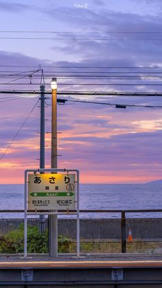 a sign that is sitting on the side of a road near the ocean with power lines above it