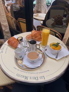 the breakfast is ready to be eaten on the table at the cafe, with orange juice and croissants