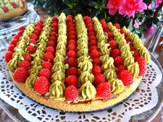 a cake decorated with raspberries and green frosting on a table next to flowers