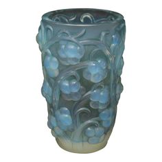 a blue glass vase with flowers and vines on the outside, sitting in front of a white background