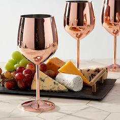 two rose gold wine goblets with cheese, grapes and crackers on a tray