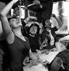 three women sitting on a bus laughing and having fun with their hands in the air