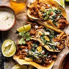 three tacos with shredded meat, cilantro and sour cream sauce on the side