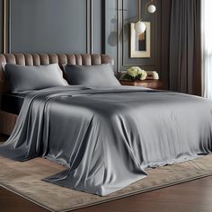 a bed with grey sheets and pillows in a room