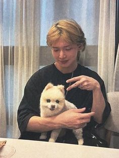 a man holding a small white dog in his lap while sitting down at a table