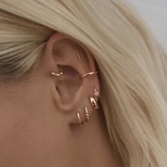 a woman with blonde hair wearing three gold ear cuffs and an earring that is shaped like a leaf