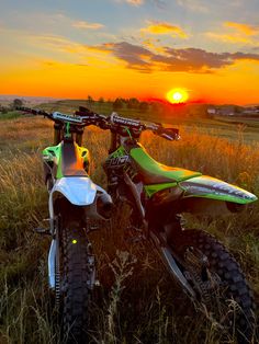 a dirt bike parked on top of a grass covered field next to the sun setting