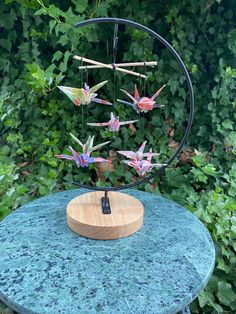 there is a sculpture made out of paper cranes on top of a table in front of some bushes