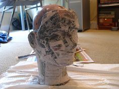 a paper mache head sitting on top of a white piece of cloth covered in newspaper