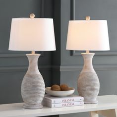 two lamps sitting on top of a white table next to a bowl of fruit and a book