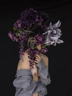 a mannequin with purple flowers on her head and hands in her hair, against a black background