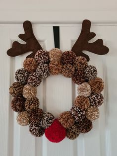 a christmas wreath with reindeer antlers hanging on the front door, decorated with brown and red yarn balls