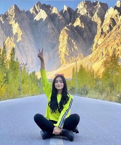 a woman sitting on the ground with her arms in the air and mountains behind her