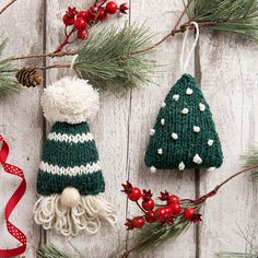 two knitted christmas ornaments hanging from a tree on a white wooden background with red ribbon