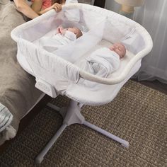 a woman sitting next to a baby in a white bassinet on top of a bed