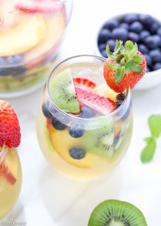 two glasses filled with fruit on top of a white table next to blueberries and strawberries