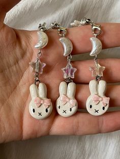 the hand is holding three charms with bunny ears and stars on them, one has a pink bow