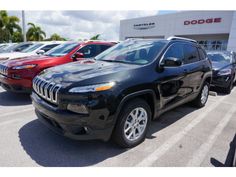 a black jeep is parked in front of a dodge dealership with other cars behind it