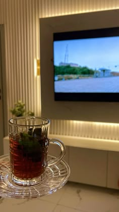 a glass cup filled with tea sitting on top of a table next to a flat screen tv