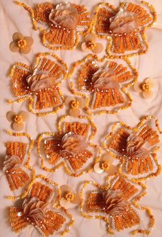 beaded flowers and beads are arranged on a white cloth with orange trimmings