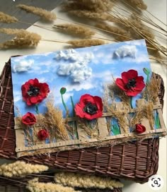 a basket with some red flowers on it next to dry grass and dried plants in the background