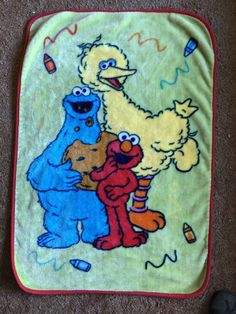 the sesame street characters are hugging each other on this green and blue blanket with red trim