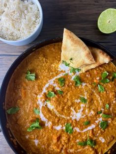 a bowl filled with curry, rice and pita bread on top of a wooden table