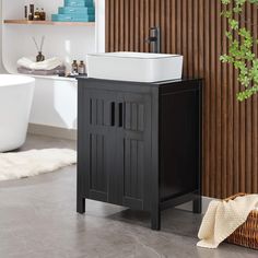 a white sink sitting next to a black cabinet and bathtub in a room with wood slats on the walls