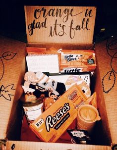 an open box filled with snacks and candy on top of a table next to a sign that says orange is glad it's fall